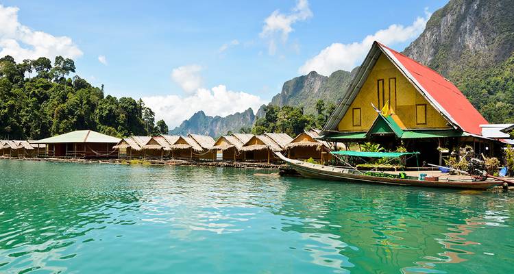Des maisons flottantes sur radeau et un bateau à longue queue sur des eaux émeraude, dominées par des falaises calcaires spectaculaires.