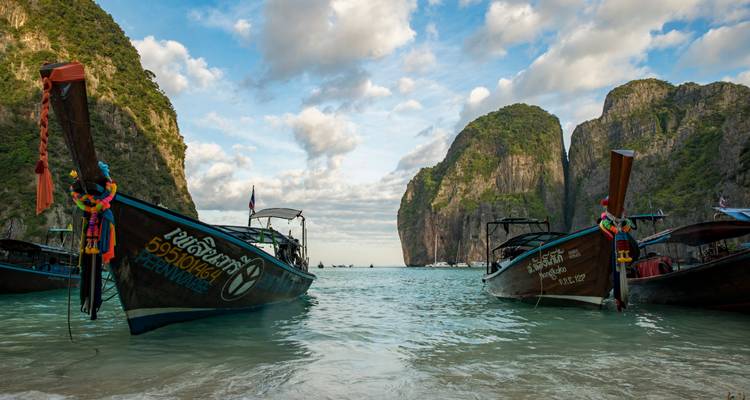 Des bateaux à longue queue ancrés dans une baie turquoise cristalline flanquée de falaises calcaires imposantes.