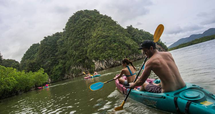 Des kayakistes pagayant entre des collines calcaires boisées sur un lagon calme.