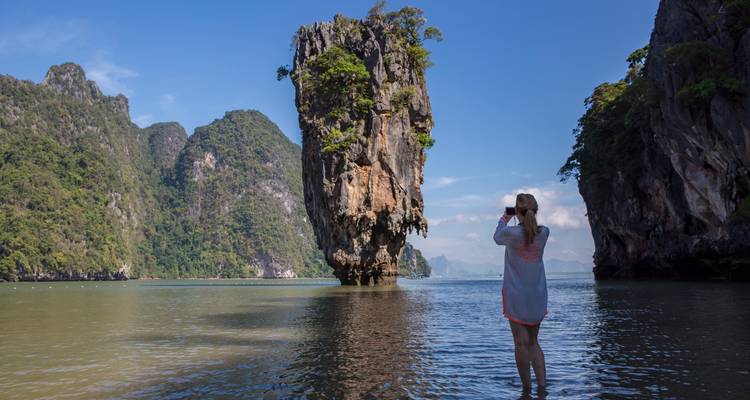 Voyageur photographiant la formation calcaire emblématique de l'île de James Bond en se tenant dans une eau peu profonde.