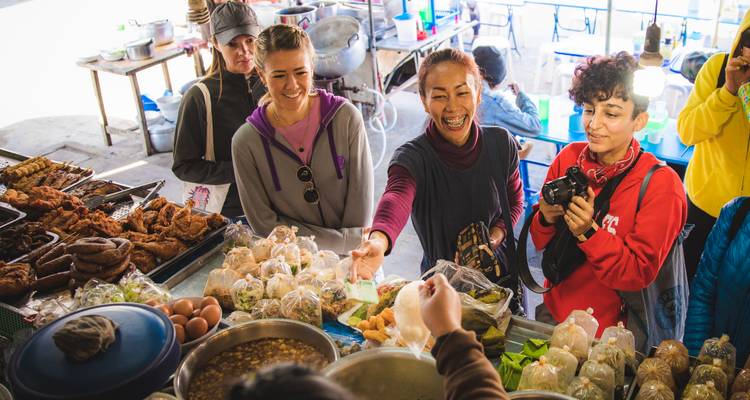 Des visiteurs riant et achetant des en-cas à un étal de marché alimentaire thaïlandais animé.