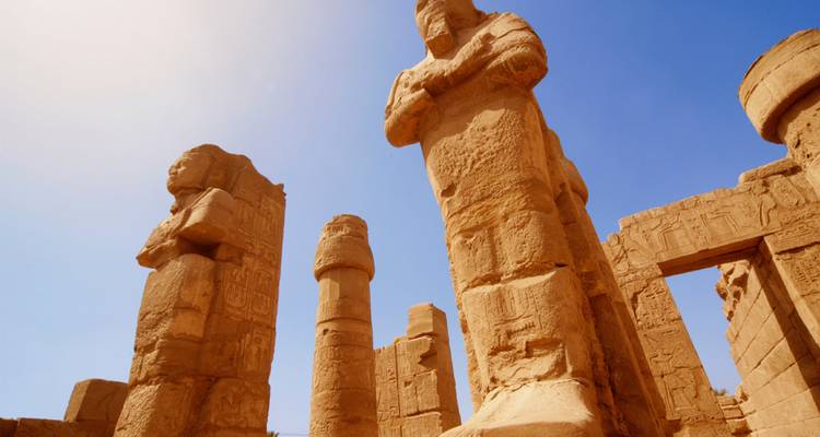 Vista de ángulo bajo de enormes estatuas de arenisca y columnas de un antiguo templo egipcio bajo un cielo azul despejado