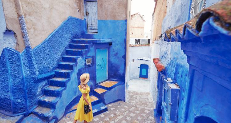 Vrouw in een gele jurk die de blauwe straten van Chefchaouen verkent.