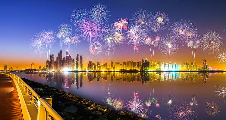 Spectacle de feux d'artifice éclatants au-dessus d'un horizon urbain se reflétant dans l'eau.