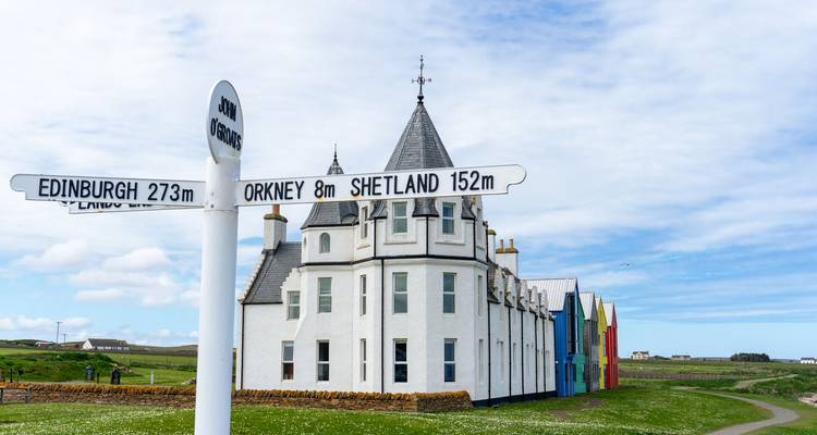 Un bâtiment avec un panneau indicateur montrant les directions vers Orkney, Shetland et Édimbourg sous un ciel lumineux.