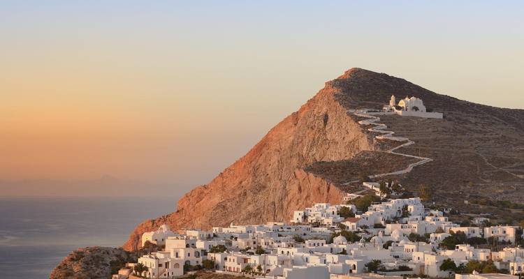 Ville perchée avec bâtiments blancs et église au coucher du soleil.