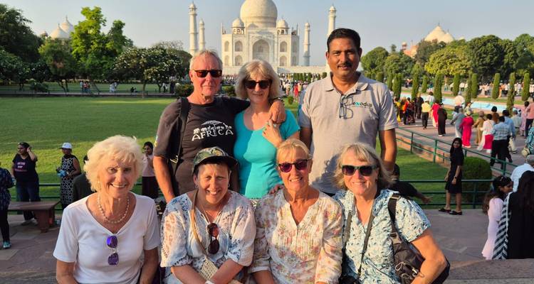 A tour group smiles in front of the Taj Mahal and its manicured gardens.