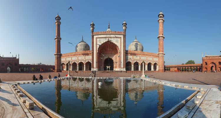 Wide panoramic view of Jama Masjid mosque with its reflection in a foreground pool.
