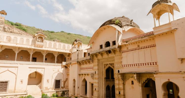 Historic Amber Fort walls and archways set against a partly cloudy sky and green hillside.