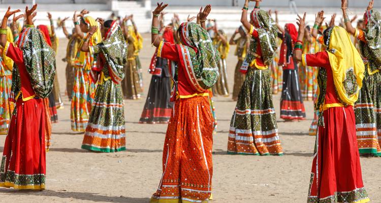 Rows of Rajasthani women in bright saris perform a traditional group dance outdoors.
