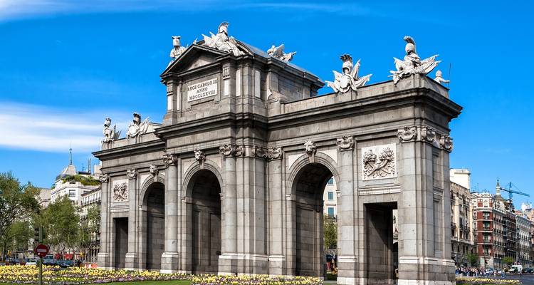 Arco triunfal de granito Puerta de Alcalá elevándose sobre los arriates de flores en Madrid.