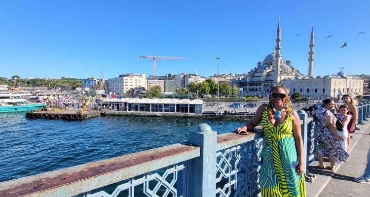 Woman posing on a bridge with a cityscape and mosque in the background.