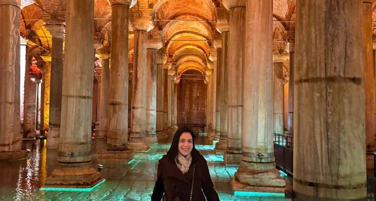 Mujer explorando la Cisterna Basílica débilmente iluminada con altas columnas iluminadas y techos abovedados de ladrillo