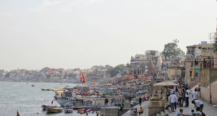 Busy riverbank with boats and buildings under a grey sky.