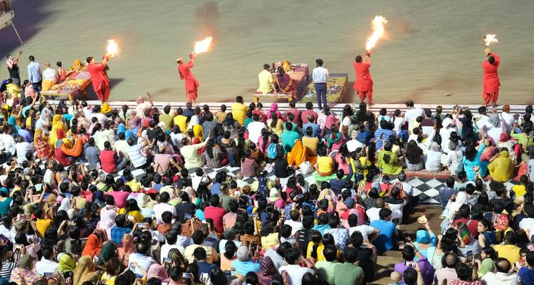 Gruppe von Menschen, die einer Flusszeremonie mit Feuer zuschaut, das von Darstellern gehalten wird.