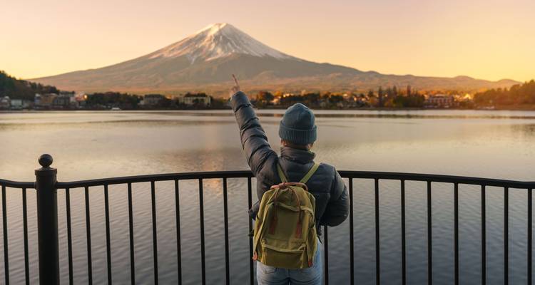 Person pointing towards Mount Fuji across a lake at sunrise.