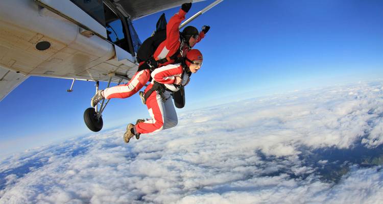 Tandemmakkers springen uit een vliegtuig hoog boven een deken van wolken onder een levendige blauwe lucht