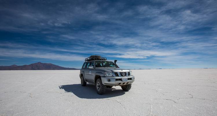 Un véhicule 4x4 se dresse seul sur l'immense étendue blanche du Salar de Uyuni en Bolivie sous un ciel bleu spectaculaire.