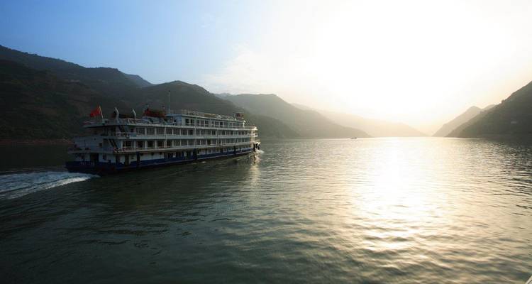 Großes Kreuzfahrtschiff, das bei Sonnenuntergang durch eine Flussschlucht fährt.