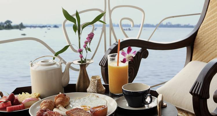 Frühstücksaufbau auf einem Tisch mit Blick auf einen Fluss mit Speisen und Getränken.