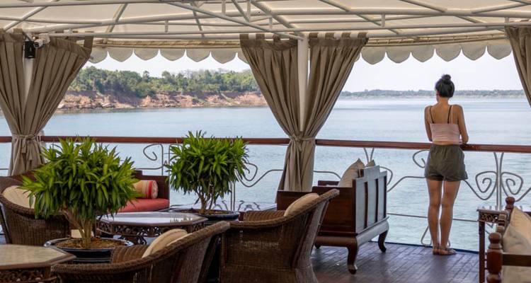 Person, die am Rand eines Flusses auf einem Kreuzfahrtdeck steht, umgeben von Möbeln.