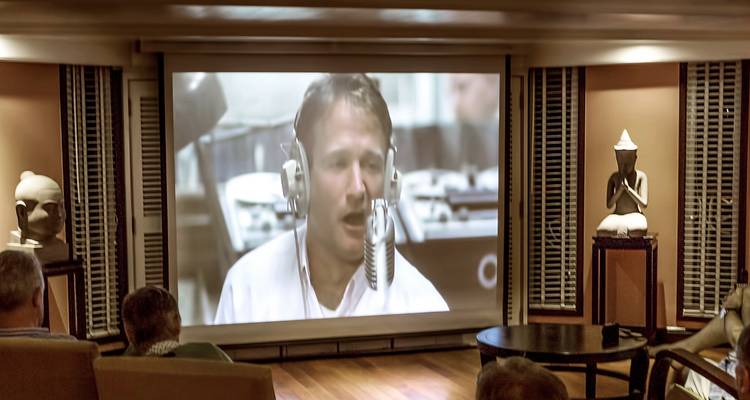 Innen-Kinoraum mit einer großen Leinwand, die eine Person zeigt, die Kopfhörer trägt.