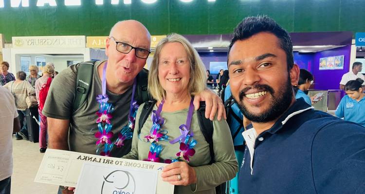 Tres personas en el área de llegadas del aeropuerto con un cartel de bienvenida.