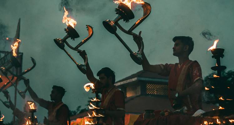 Groep mannen die een traditionele avond-aarti uitvoeren bij de rivier.
