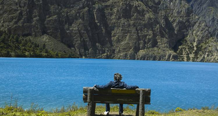 Personne assise sur un banc au bord d'un lac bleu.