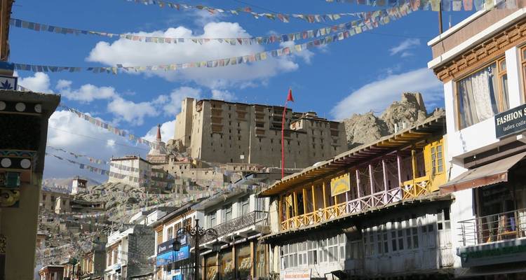 Straatbeeld met gebouwen en gebedsvlaggen in Leh, met structuur op de heuveltop.