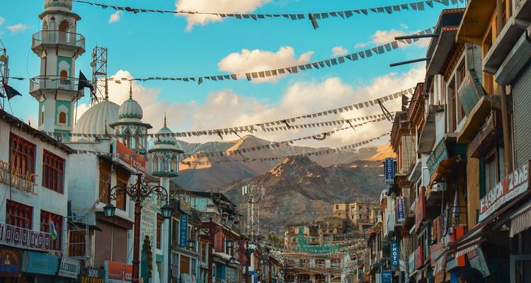Drukke straat in Leh met bergen op de achtergrond onder gebedsvlaggen.