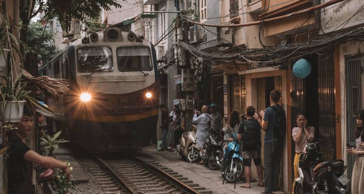 Een trein die door een smalle straat rijdt met mensen en scooters.