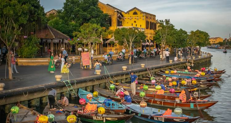 Boten met kleurrijke lantaarns langs een rivier in Hoi An met mensen die in de buurt wandelen.