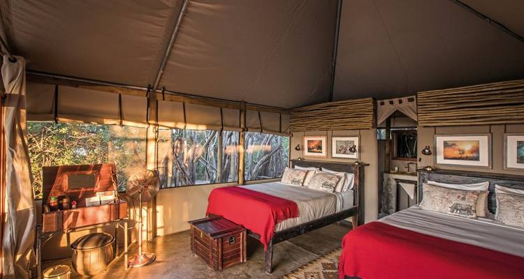 Interior of a safari tent with two beds and wooden decor.