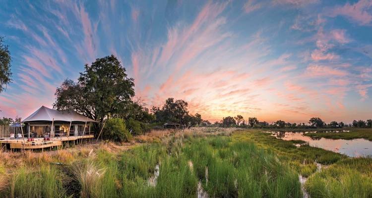 Scenic landscape with tents and a dramatic sunset in the Okavango Delta.