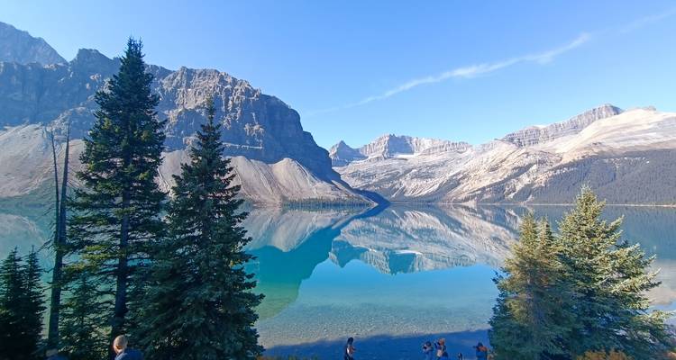 Menschen, die eine Aussicht auf einen großen blauen See mit Spiegelung genießen, umgeben von Bergen.