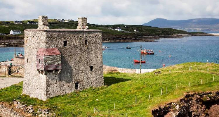 Old stone tower by a vibrant coastal area.