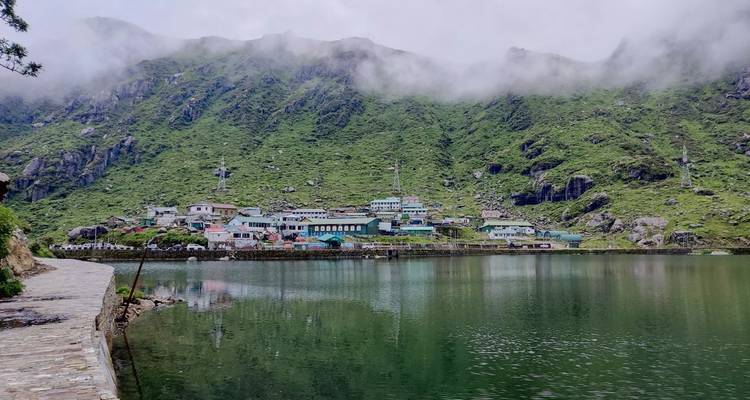Una vista junto al lago con montañas brumosas y edificios coloridos.
