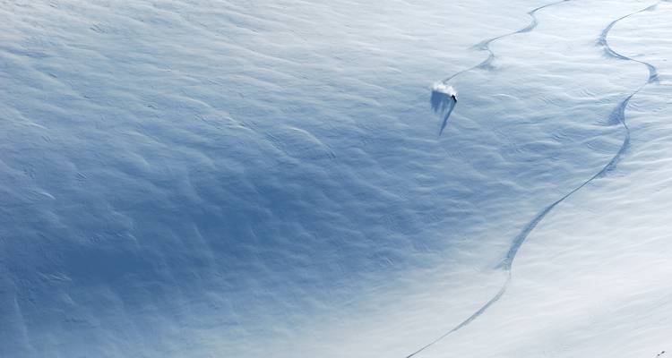 Un skieur solitaire sur une vaste pente enneigée.