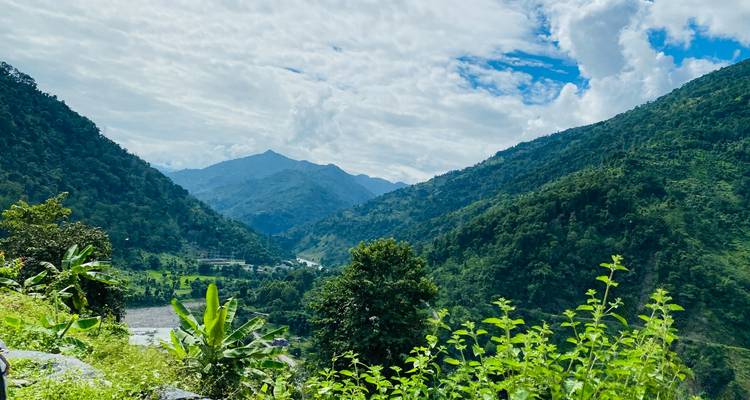 Vallée pittoresque avec des collines verdoyantes et un ciel nuageux.