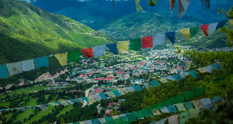 Des drapeaux de prière multicolores encadrent une vallée verdoyante qui s'étend à perte de vue et une ville lointaine sous un ciel bleu cristallin de l'Himalaya.