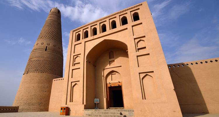 Un minaret en adobe qui s'élance se dresse à côté d'une entrée voûtée contre un ciel bleu vif.