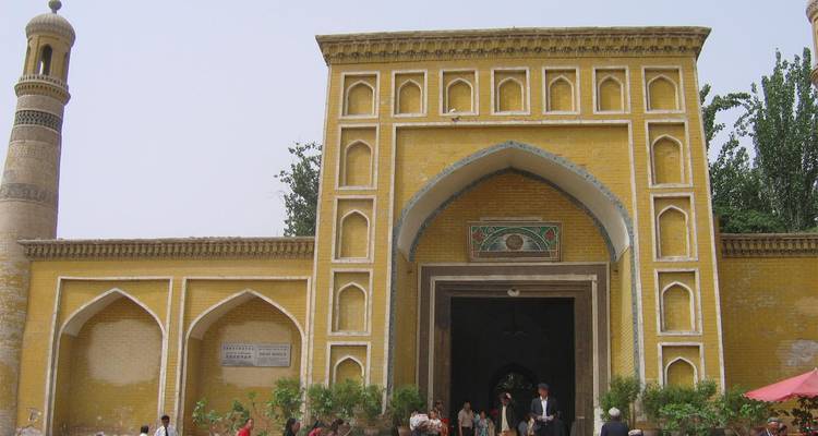 Mezquita Id Kah de ladrillo amarillo con entrada arqueada bullendo de visitantes bajo un cielo pálido.