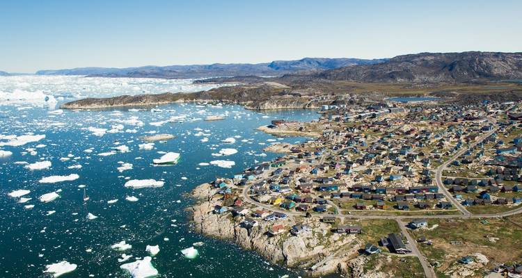 Vista aérea del pueblo de Ilulissat rodeado de aguas llenas de hielo y un paisaje accidentado.
