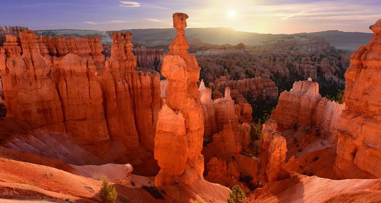 La salida del sol ilumina los altos hoodoos del Cañón Bryce con rayos brillando sobre las dramáticas agujas de roca roja.