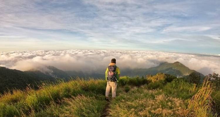Personne contemplant les nuages et les montagnes, en randonnée avec sac à dos.