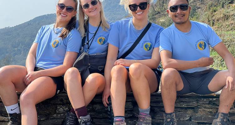 Menschen sitzen im Freien und tragen passende Hemden vor einer Bergkulisse.