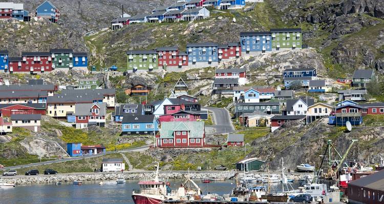 Petite ville sur les hauteurs aux maisons en bois aux couleurs vives surplombant un port très animé dans le sud du Groenland.