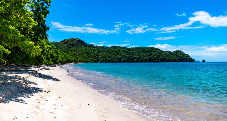 Sandstrand mit grünen Hügeln und blauem Ozean.