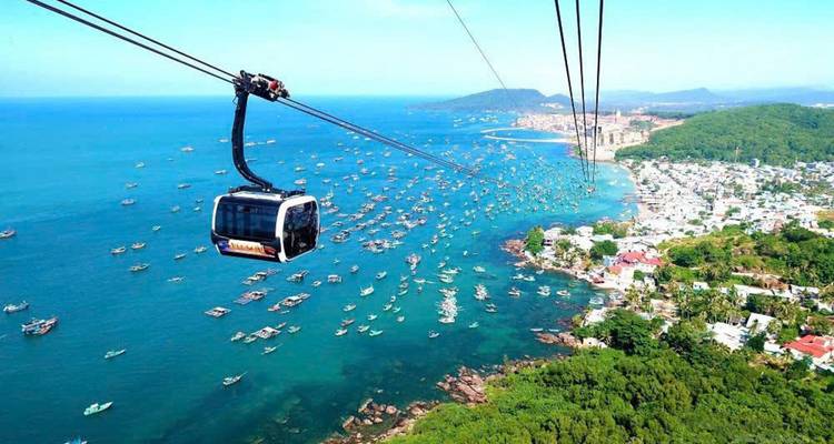 Cable car over a blue sea with boats and coastal views.
